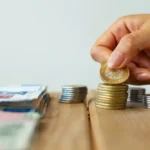 Persona apilando una pequeña cantidad de pesos, representando finanzas ajustadas