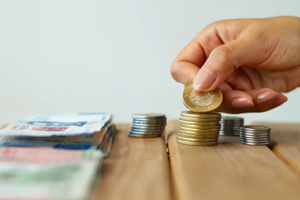 Persona apilando una pequeña cantidad de pesos, representando finanzas ajustadas